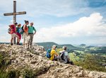 Eine Gruppe Menschen schaut vom Gipfelkreuz aus ins Tal
