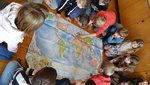 Kinder sitzen um eine Weltkarte und erarbeiten ein Klimaschutzprojekt